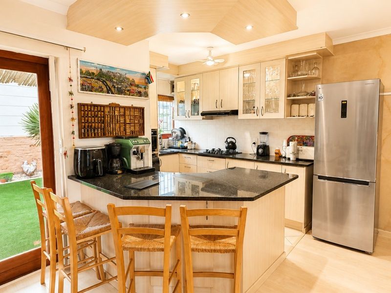 Open-plan kitchen featuring granite countertops, built-in cabinetry, and a gas hob, with direct access to an outdoor patio area through wooden doors.