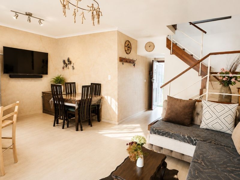 Open-plan living and dining area featuring a staircase, kitchen island, and light-toned laminate flooring in a well-maintained apartment setting.