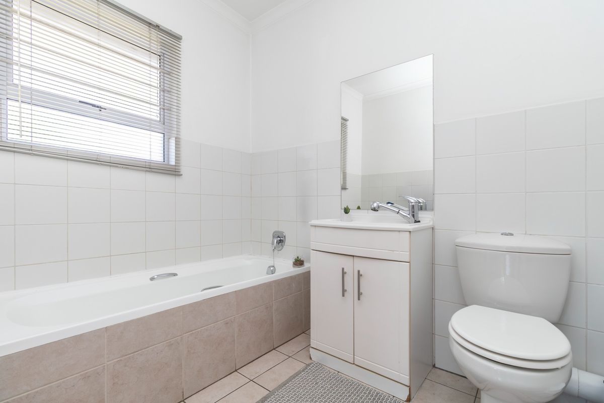 A functional bathroom featuring a bathtub, vanity with basin, toilet, and neutral wall and floor tiling with a window for natural light.