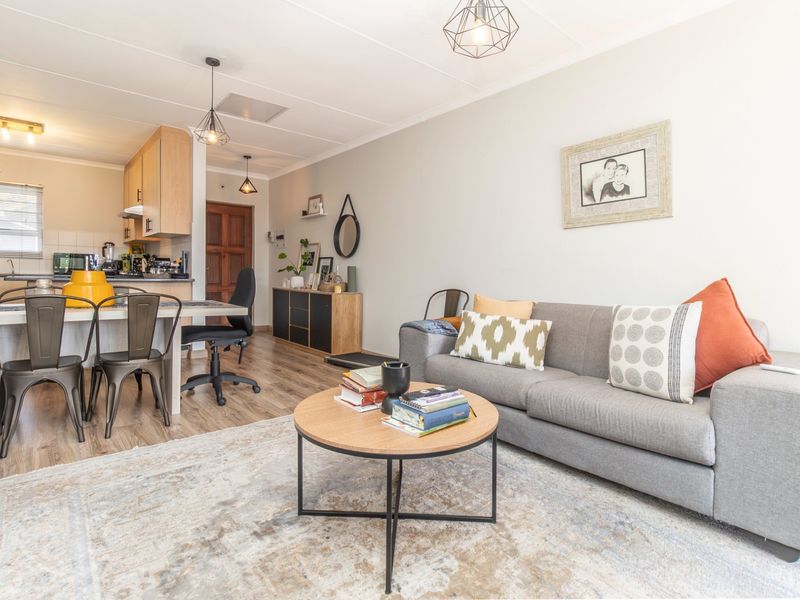 An open-plan living and kitchen area featuring laminate flooring, modern pendant lighting, and functional built-in kitchen cabinetry.