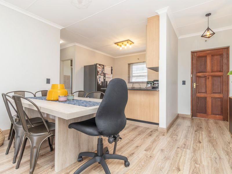 Open plan living and dining area featuring laminate flooring, a wooden entrance door, and a functional kitchen with built-in cabinetry.