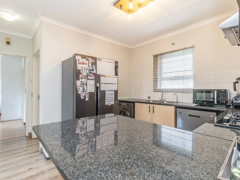 A functional kitchen featuring granite countertops, ample cabinetry, a built-in hob, and an extractor fan, with a tiled backsplash and neutral finishes.