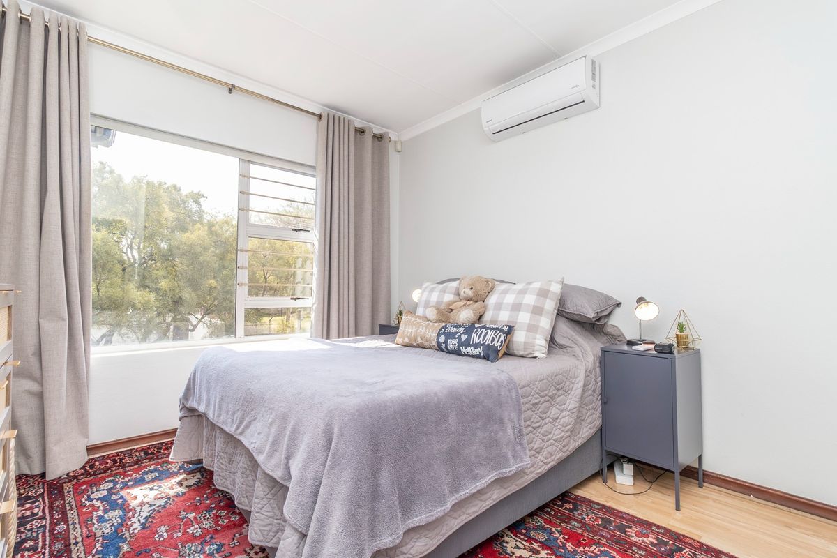 A bright and well-maintained bedroom featuring laminate flooring, a large window for natural light, and a wall-mounted air conditioning unit.