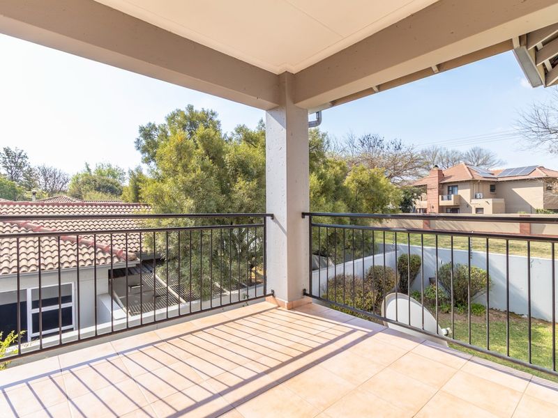 A spacious covered balcony featuring tiled flooring and a secure metal balustrade, offering an open view of the surrounding residential area.