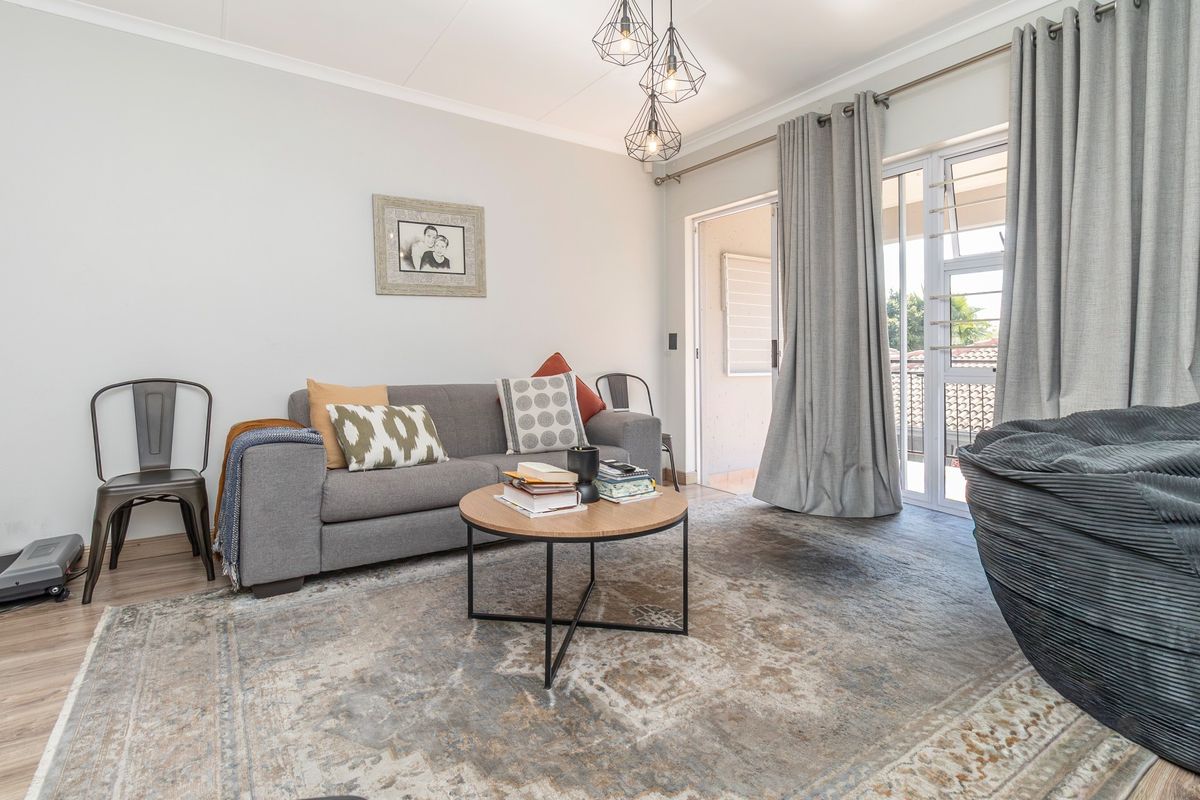 A bright living room featuring laminate flooring, modern pendant lighting, and a sliding glass door providing access to an outdoor balcony area.