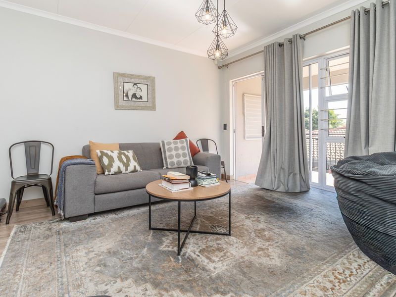 A bright living room featuring laminate flooring, modern pendant lighting, and a sliding glass door providing access to an outdoor balcony area.