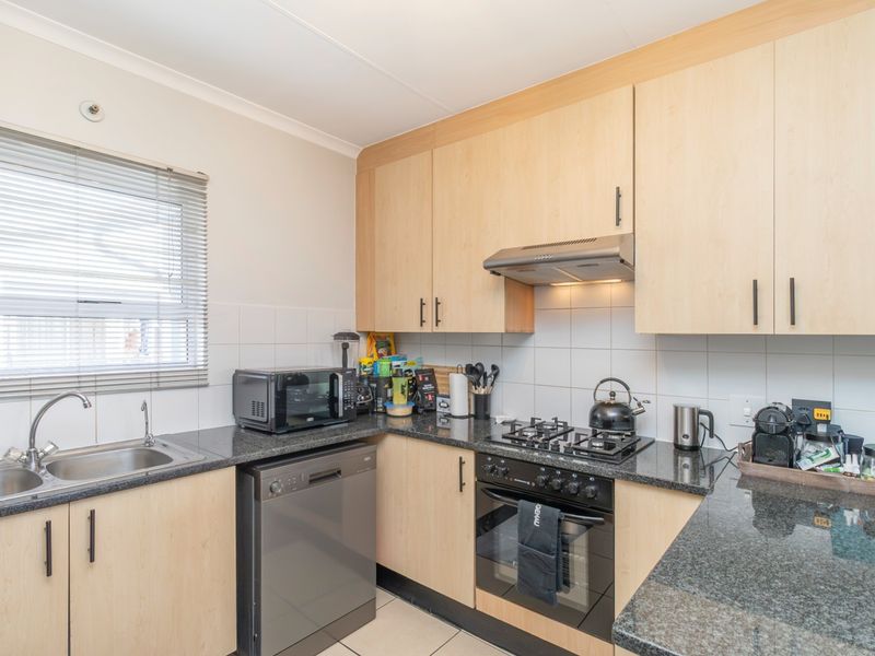 Functional kitchen featuring light wood-finish cabinetry, granite countertops, a gas hob, built-in oven, and a tiled backsplash with a window for natural light.
