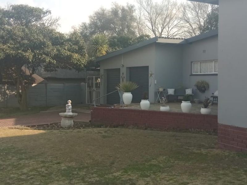 Rear view of the property featuring a paved driveway, lawn, brick retaining wall, and double garage access.