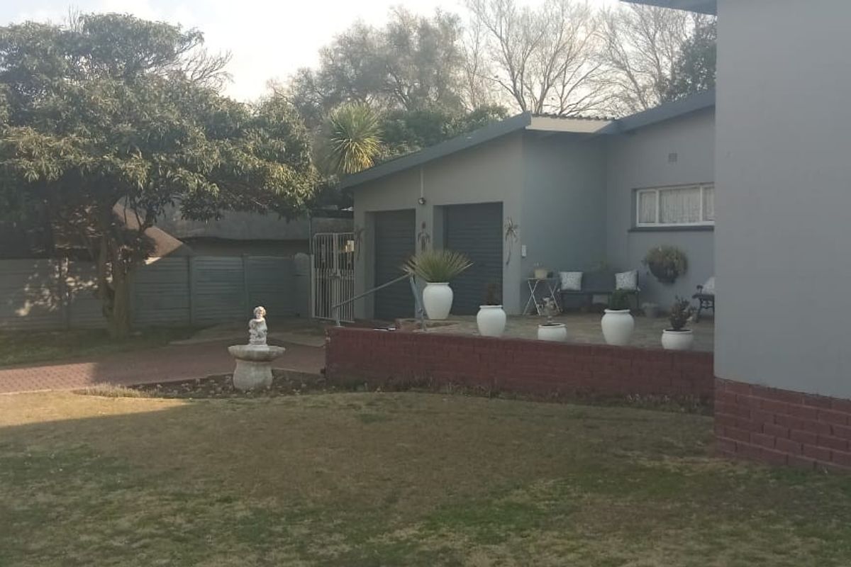 Rear view of the property featuring a paved driveway, lawn, brick retaining wall, and double garage access.