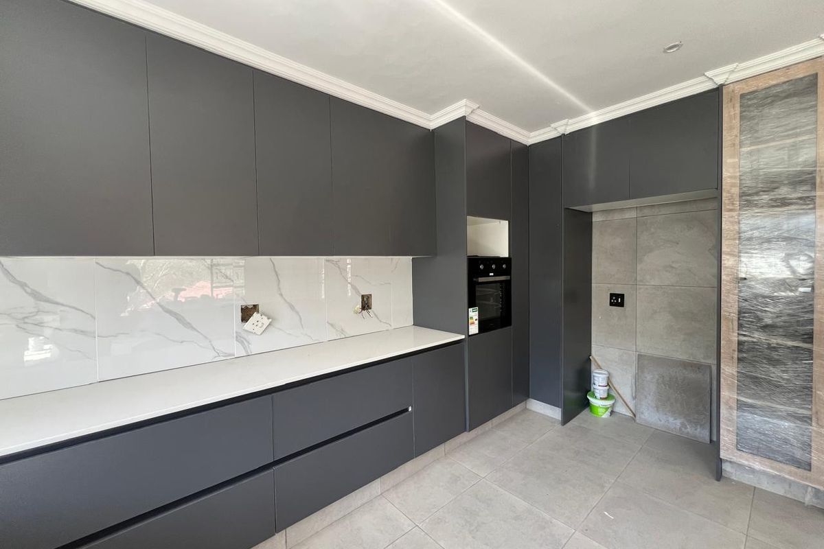 Modern kitchen featuring dark grey cabinetry, marble-look splashback, stone countertops, and built-in oven, currently awaiting final electrical and finishing touches.