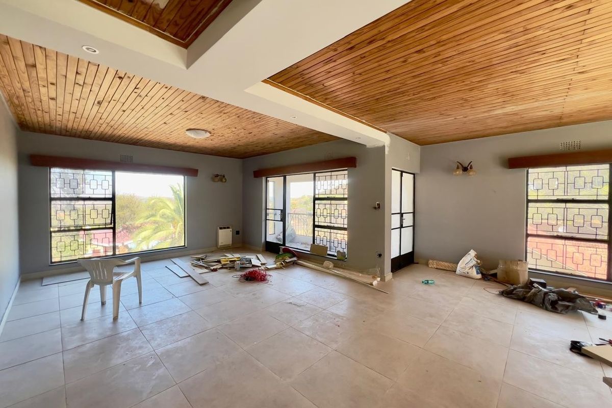 Spacious living area featuring a timber-clad ceiling, large windows with security bars, and tiled flooring, currently undergoing renovation.