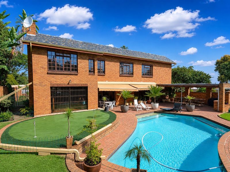 Rear view of a double-story brick house featuring a swimming pool, artificial putting green, and a covered patio area with a retractable awning.