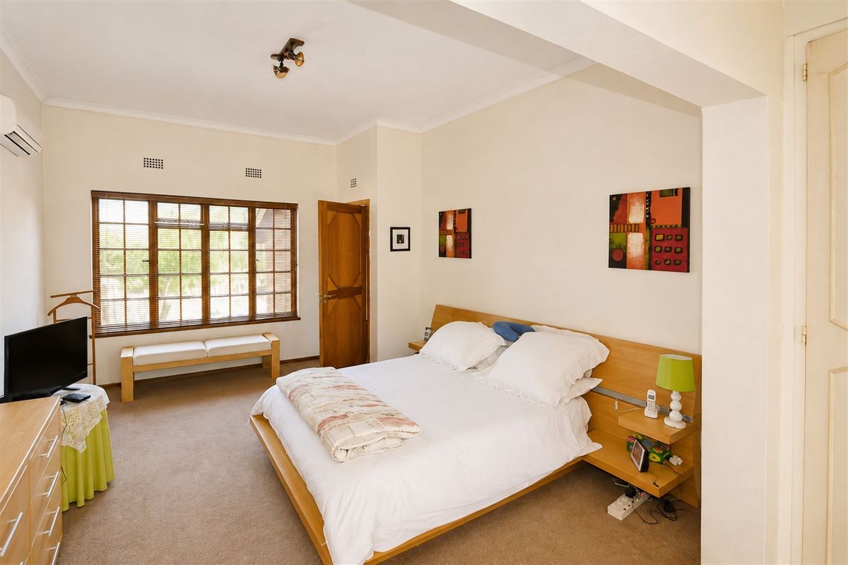 A well-lit bedroom featuring carpet flooring, a timber-framed window, and a wall-mounted air conditioning unit.