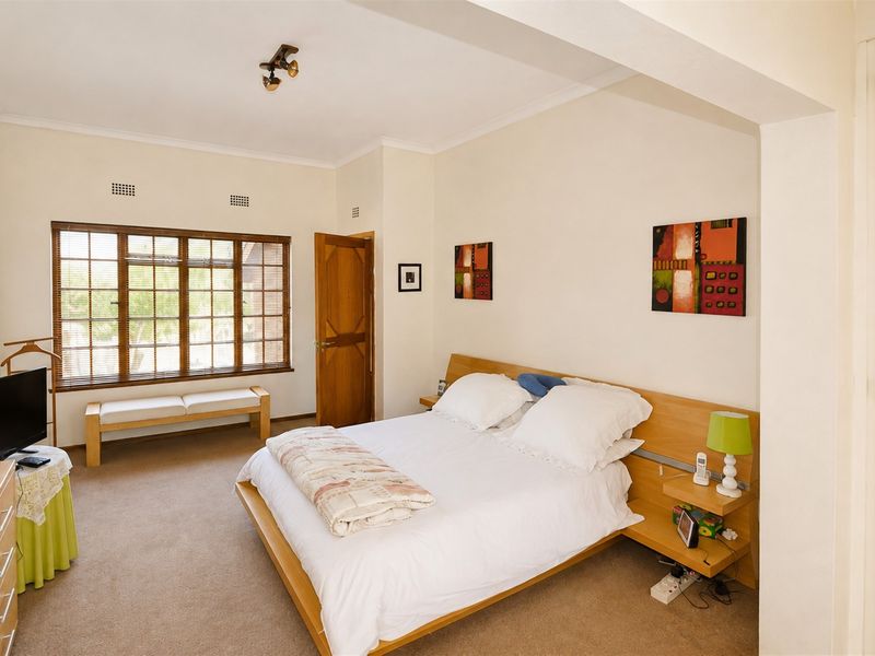 A well-lit bedroom featuring carpet flooring, a timber-framed window, and a wall-mounted air conditioning unit.