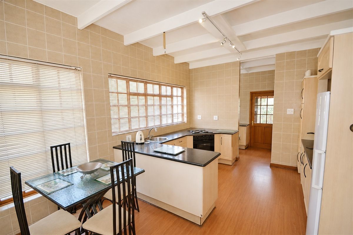A functional kitchen featuring light-toned cabinetry, dark laminate countertops, built-in cooking appliances, and a tiled splashback with exposed beam ceilings.