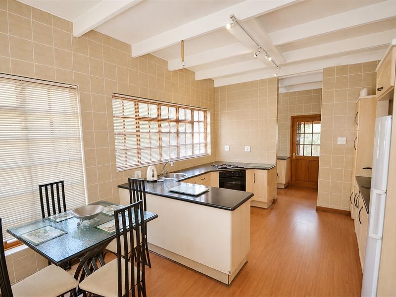 A functional kitchen featuring light-toned cabinetry, dark laminate countertops, built-in cooking appliances, and a tiled splashback with exposed beam ceilings.