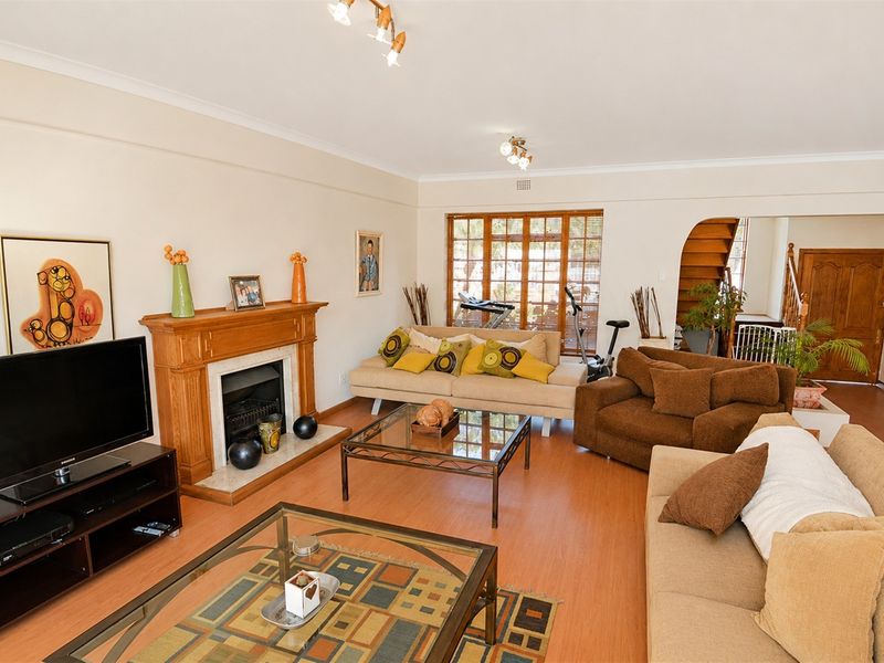 Spacious living room featuring a traditional fireplace with a timber mantelpiece, laminate flooring, and large timber-framed windows allowing natural light.