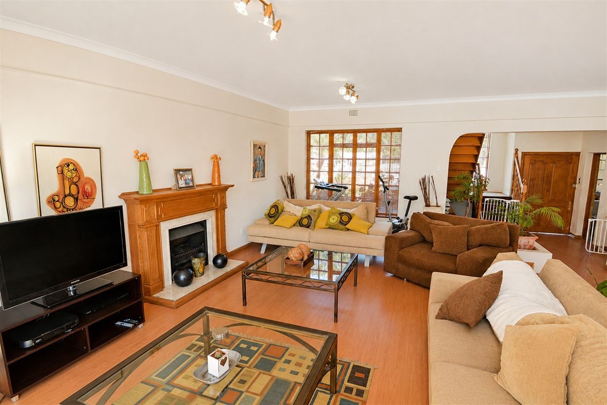 Spacious living room featuring a traditional fireplace with a timber mantelpiece, laminate flooring, and large timber-framed windows allowing natural light.
