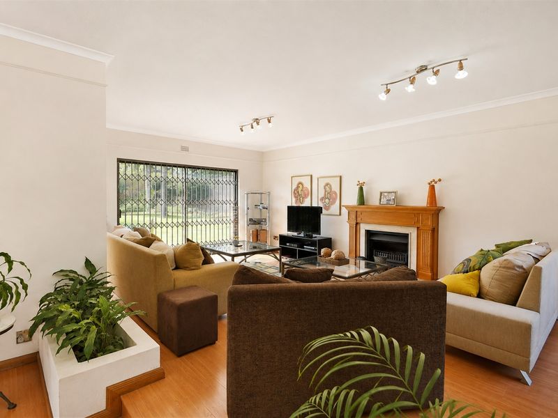 Spacious living room featuring laminate flooring, a classic fireplace with a wooden mantel, and sliding glass doors leading to the garden.