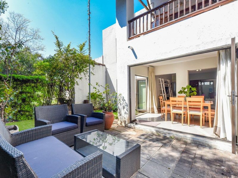 Rear exterior view featuring a paved patio area, garden, and folding glass doors providing seamless access to the indoor dining space.