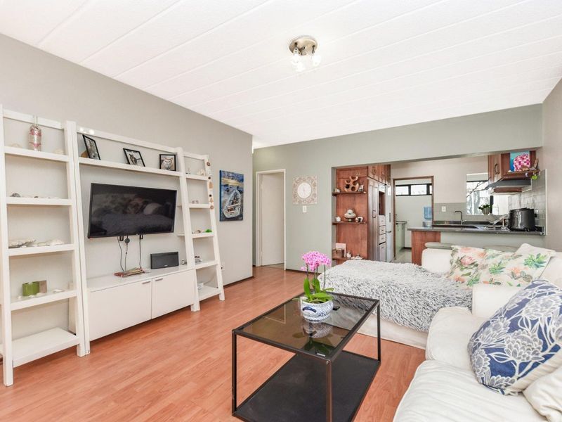 Open-plan living area featuring laminate flooring and a connected kitchen with built-in cabinetry and functional workspace.