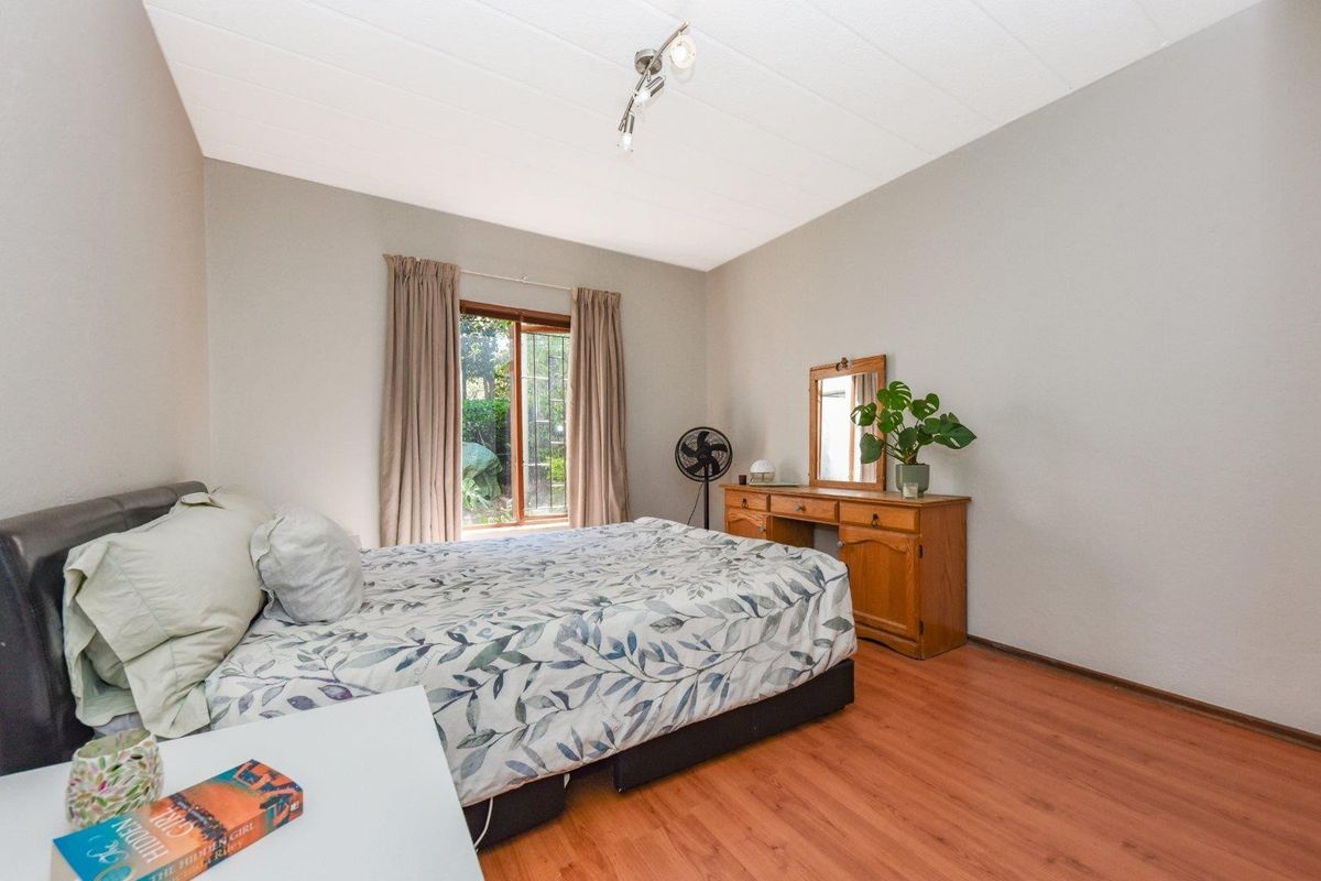 A well-lit bedroom featuring laminate flooring, a window with security bars, and a modern ceiling-mounted spotlight fixture.