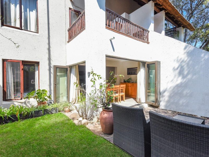 Rear view of the apartment featuring a private garden, paved patio area, and access to the interior through double glass doors.