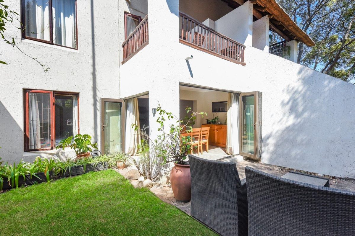Rear view of the apartment featuring a private garden, paved patio area, and access to the interior through double glass doors.