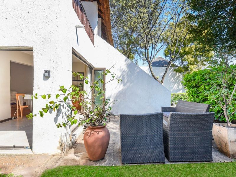 A private paved patio area featuring sliding glass door access to the interior, set against a landscaped garden backdrop.