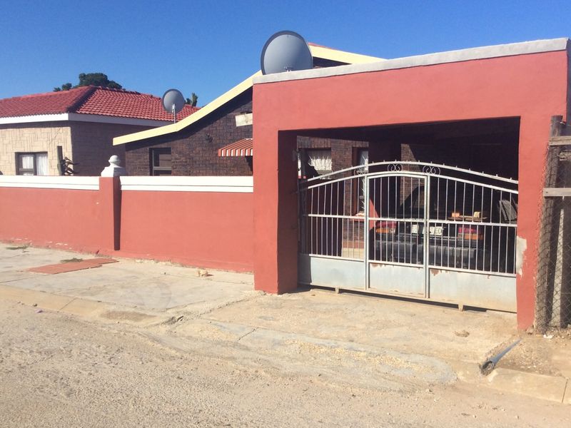 Front view of the property featuring a perimeter wall, metal driveway gate, and a covered carport area.
