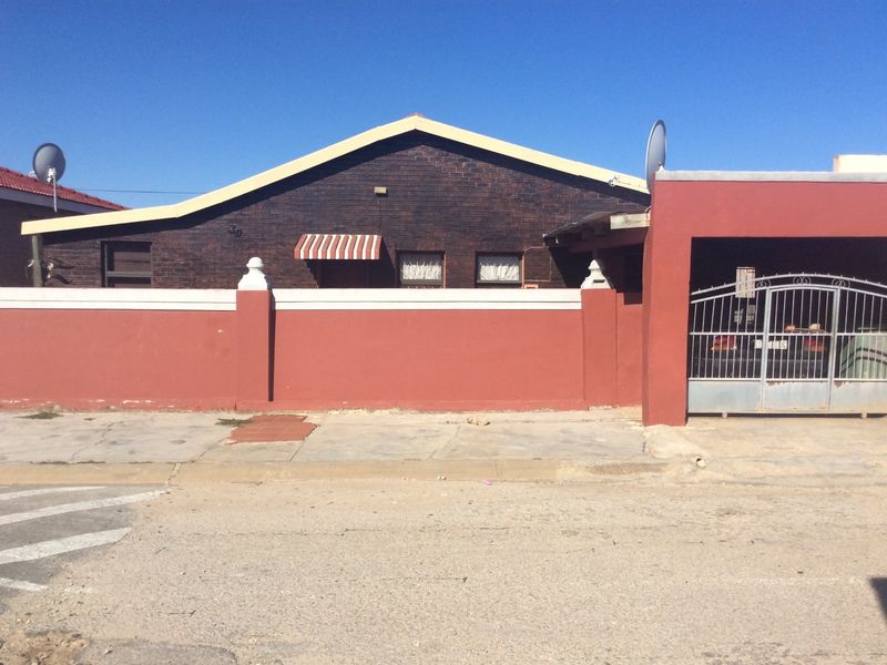 Front elevation of a brick house featuring a perimeter wall, gated carport, and satellite dish installation.