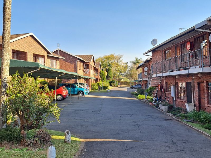 Exterior view of an apartment complex featuring brick buildings, covered parking bays, and paved driveway access.