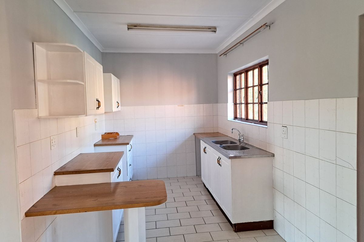A functional, empty kitchen featuring white built-in cabinetry, laminate countertops, a double stainless steel sink, and tiled splashbacks with neutral floor tiles.