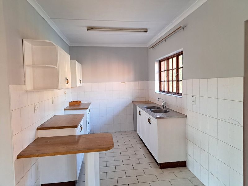 A functional, empty kitchen featuring white built-in cabinetry, laminate countertops, a double stainless steel sink, and tiled splashbacks with neutral floor tiles.