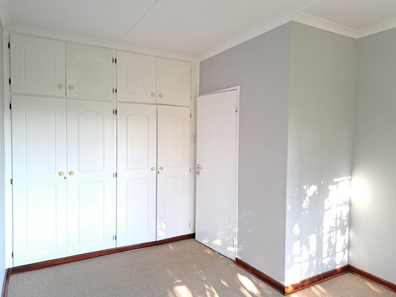 A clean, empty bedroom featuring ample built-in cupboard storage, neutral wall finishes, and carpeted flooring.