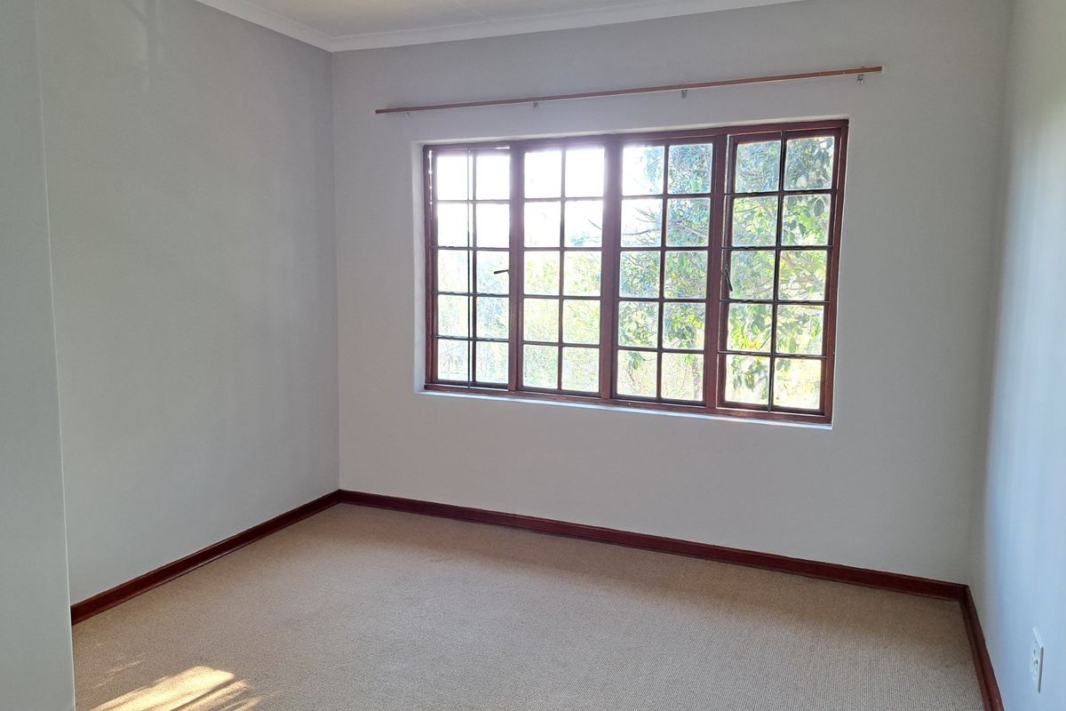 A bright, empty bedroom featuring neutral walls, carpeted flooring, and large wooden-framed windows that allow for natural light.