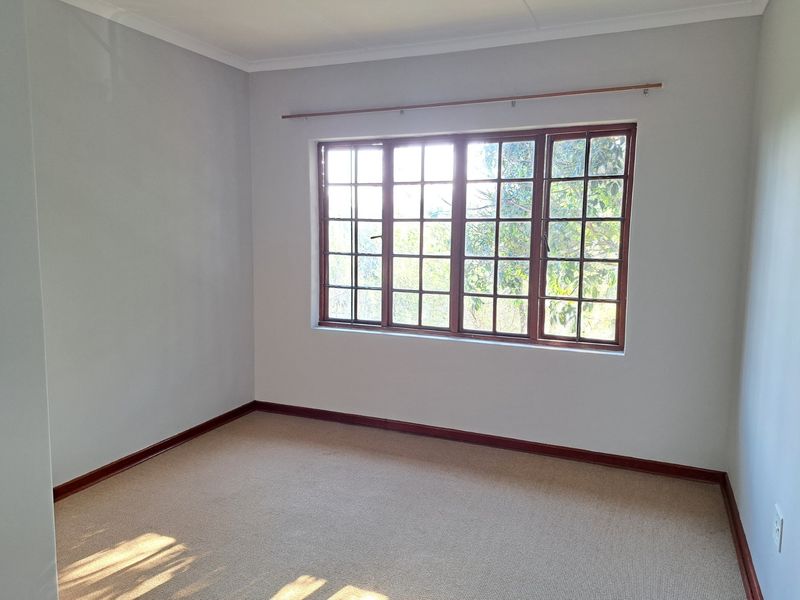 A bright, empty bedroom featuring neutral walls, carpeted flooring, and large wooden-framed windows that allow for natural light.