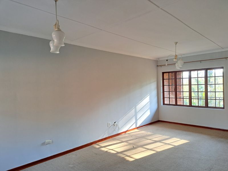 A bright, empty living room featuring carpet flooring, timber-framed windows, and classic pendant lighting, offering a blank canvas for personalization.
