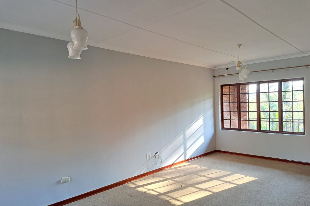 A bright, empty living room featuring carpet flooring, timber-framed windows, and classic pendant lighting, offering a blank canvas for personalization.