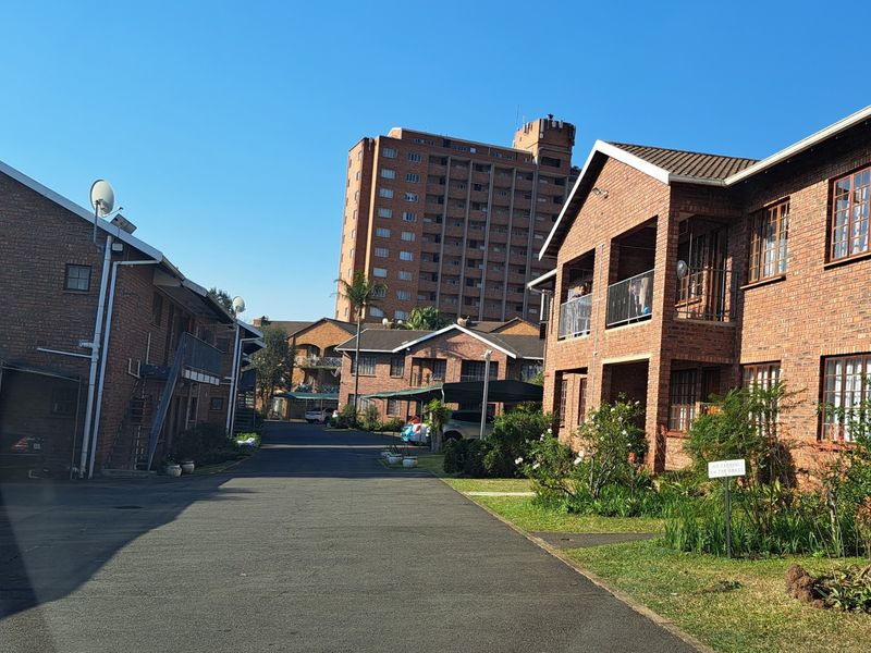 Exterior view of a residential apartment complex featuring brick buildings, paved driveways, and covered parking areas under a clear blue sky.