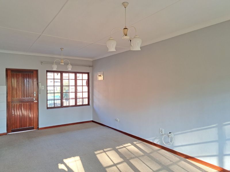 A spacious, empty living room featuring neutral walls, carpeted flooring, and a timber-framed window, offering a blank canvas for interior design.