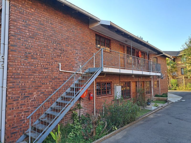 Exterior view of a multi-story apartment building featuring face brick construction, an external metal staircase, and a balcony with safety equipment.