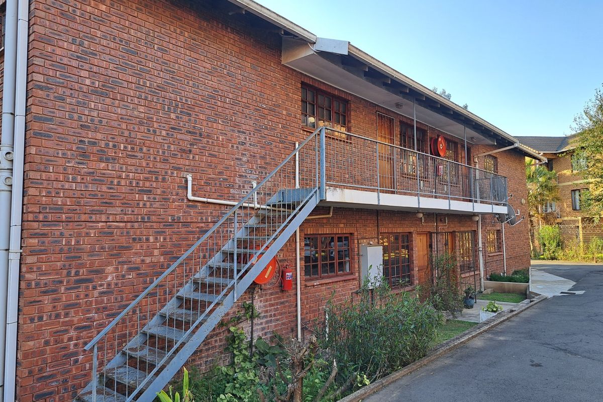 Exterior view of a multi-story apartment building featuring face brick construction, an external metal staircase, and a balcony with safety equipment.