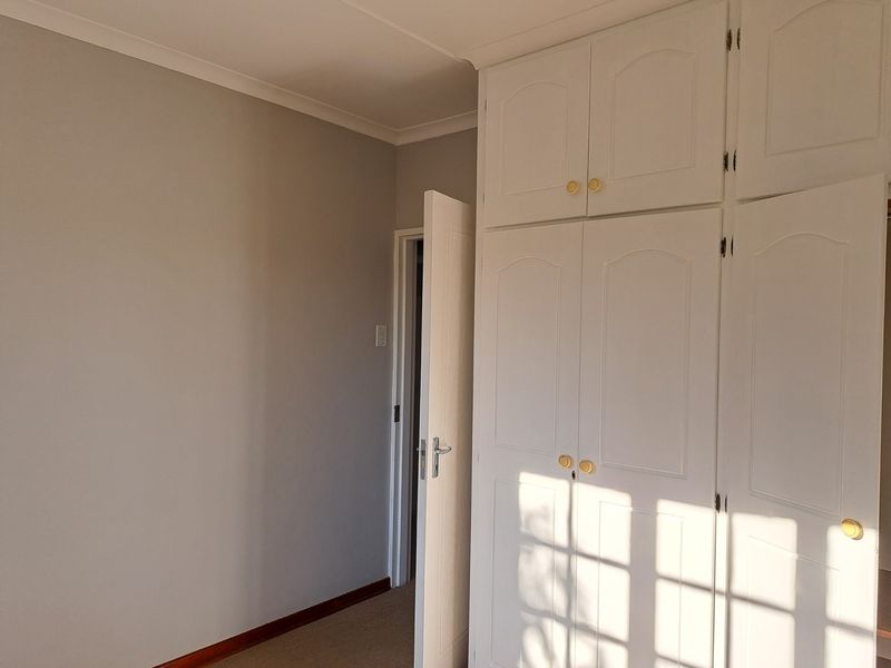 A bright, empty bedroom featuring neutral walls, carpeted flooring, and ample built-in cupboard storage with overhead cabinets.