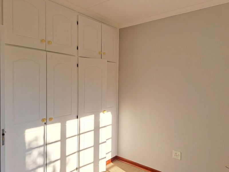 A bright, empty bedroom featuring white built-in cupboards with classic panel detailing and neutral wall finishes.