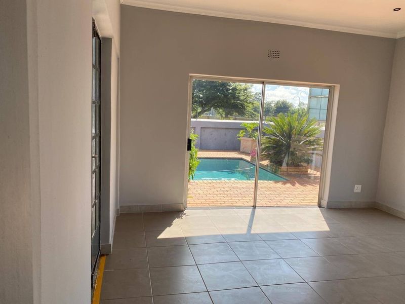 An empty living room featuring neutral tiled flooring and a large sliding glass door providing direct access to the outdoor pool area.
