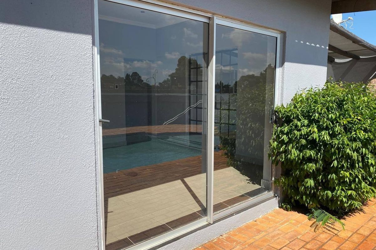 Rear exterior view featuring a sliding glass door opening onto a brick patio with a swimming pool in the background.