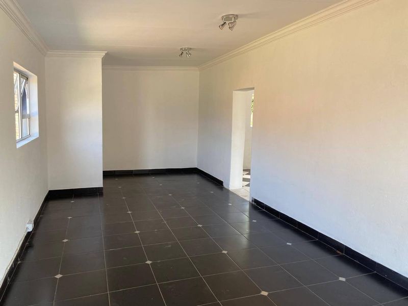 A bright, empty living room featuring dark tiled flooring, white walls, ceiling cornicing, and modern spotlight fixtures.