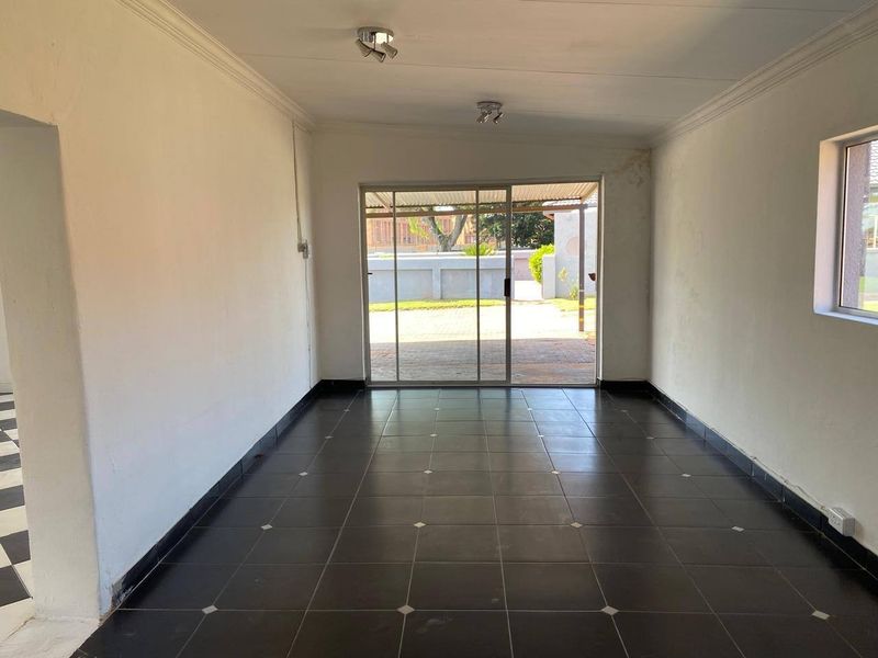 An empty living room featuring dark ceramic floor tiles, coved ceilings, and a sliding glass door providing access to the exterior.