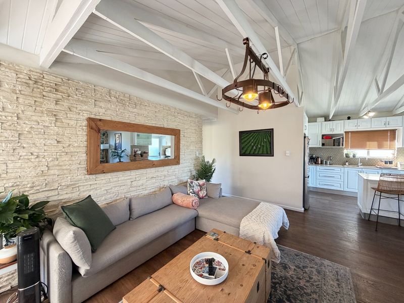 Spacious open-plan living area featuring a vaulted ceiling with exposed trusses, a stone feature wall, and a modern kitchen with shaker-style cabinetry.